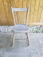 Front view of the wooden chair showing the backrest with vertical slats and the seat with scratches.