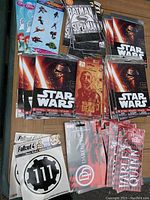Photo showing multiple unopened packs of temporary tattoos and sticker sets with popular themes such as Star Wars, Batman, Superman, Fallout 4, Daredevil, and The Walking Dead.