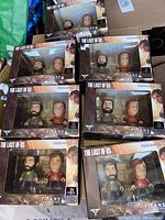 Seven boxed The Last of Us Titans Vinyl Figure sets featuring Joel and Ellie in a stylized vinyl design.