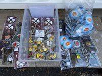 Wide view of 104 enamel metal collector pins in various designs, some displayed loose inside a tray and others packaged individually in plastic bags or on branded backing cards.