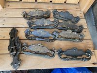 Vintage cabinet drawer pulls and one door knocker laid out on a wooden surface, showing the full set in rustic, heavily used condition.
