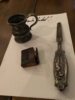 Full view of antique nail file, small metal jug, and miniature Bible together on a table: shows overall condition and size relation
