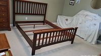 Overall side view of the wooden bed frame with slatted head and footboards in a bedroom setting.