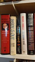 Spine view of several hardcover and paperback books including Herberge Dragons, Inside & Out, The Burning Room, and The Runaway Jury.