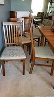 Set of four wooden flat back chairs arranged in living room, fabric seats light beige with woven pattern.