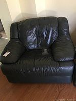 Front view of dark green oversized Italian leather armchair showing padded arms and backrest with some creases and wear marks on leather surface