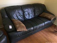 Full view of the dark green Italian leather sofa from the front angle showing cushions and one throw pillow on each end.