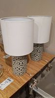 Pair of ceramic base table lamps with white fabric drum shades placed side by side on a wooden surface.