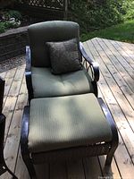 Full view of the patio chair with sage green cushion and paisley throw pillow on wooden deck outdoors.