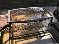 Full view of the rectangular patio table showing the glass top, metal frame, and wicker lower shelf