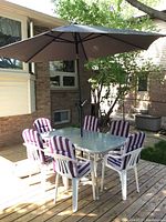 Full patio set showing the table, six cushioned plastic chairs, large patio umbrella, and base on wooden deck outdoors in daylight.