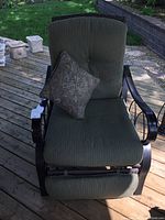 Front view of the reclining patio chair showing sage green cushions and metal frame with a paisley throw pillow.