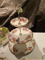 Full view of three-tiered serving plate set showcasing floral porcelain plates with gold trim and metal gold-tone rod and handle.