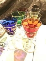 Front angle image showing five colored crystal glasses with gilt trim and one colored glass without gilt.
