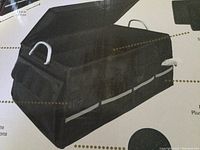 Photo showing black foldable trunk organizer with metal handles and reflective white strips on sides, dimensions shown as 23.6 x 14 x 12 inches.