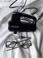 Black & Decker handheld mixer in black with cord and three attachments placed on white background.