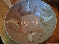 Top view of round pottery plate showing four stylized birds in white and brown colors, with concentric circles at center.