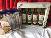 Four bottles of La Dolce Vita organic flavored extra virgin olive oils in original box next to Trudeau gourmet salts set package