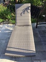 Front view of the outdoor lounger showing woven synthetic wicker material and flat position.