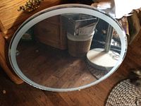 Front view of a large round mirror with a lighted frame resting on a wooden floor.