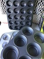 Stack of assorted baking muffin tins including 12-cup and 6-cup sizes in black and silver colors.
