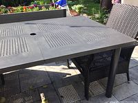Outdoor rectangular patio table with removable legs and perforated square pattern surface beside two black woven wicker chairs.