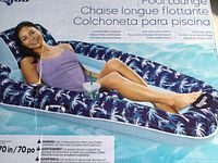 Photo of the pool lounger with a person lying on top, showing the printed palm tree pattern and drink holder.