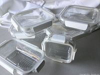 Several Snap Lock Clear food storage containers stacked and arranged showing clear plastic bodies and white snap-lock lids with gray tabs