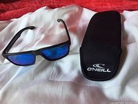 Top down view showing sunglasses and soft-sided zippered black O'Neill case with logo