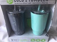 Two insulated tumblers in packaging, dark gray and teal colors, with lids and straws visible.