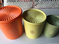 Three round vintage Tupperware canisters in orange, yellow, and green, shown side by side on table.