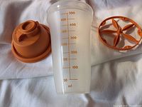 Photo of the vintage Tupperware shaker disassembled showing the transparent measuring container, orange lid, and internal spinner.
