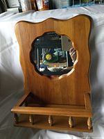 Overall front view of the vintage wooden wall mirror showing decorative shaped frame, small shelf with spindles, and central mirror glass.