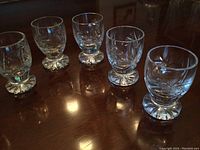 Six Pinwheel crystal liqueur glasses grouped on wooden table, showing size and cut pattern.