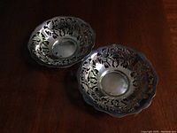 Two silver candy bowls with grapevine design shown from above on dark wood surface.