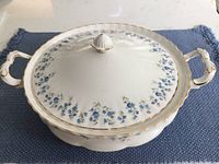 Covered vegetable bowl with lid on blue placemat showing floral design and gold trim