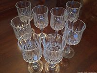 Eight crystal wine glasses arranged on a wooden table, showing their diamond-cut pattern and clarity.
