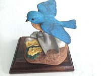 Porcelain bluebird figurine on wooden base, showing bright colors and detailed spring planting scene from front side.
