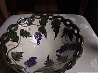 Top and angled view showing the hand-painted grapes and leaves inside the scalloped edge bowl with green cut-out rim design.