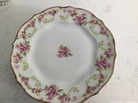 Close-up of a single antique Limoges dessert plate showing scalloped edge, pink rose floral pattern, and gold rim.