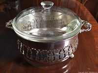 Full view of the glass casserole dish inside the silver carrier, showing the complete set including lid and handles.