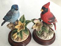 Both bird figurines on circular wooden stands showing details and colors.