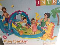 Box image showing children playing in inflatable Dinoland Play Center with dinosaur-themed decorations and slide.
