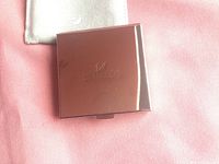 Closed compact with smooth side showing engraved Swarovski logo and pouch beneath.