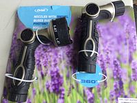 Two black and gray Orbit swivel nozzles for garden hose on purple floral retail backing. Each nozzle has a rotating dial to adjust spray patterns and 360-degree swivel feature.