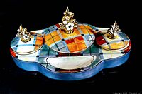 Front view of the antique Noritake double inkwell showing colorful geometric hand painted pattern and gold-toned floral finials on lids.