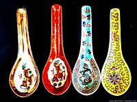 Photo showing four vintage Chinese porcelain soup spoons with distinct traditional dragon and cloud patterns in various colors (brown, red, blue, yellow) against black background.