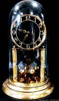 Photo of a vintage mantel clock under a glass dome with gold-tone decorative elements, clock face, and rotating pendulum.