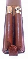 Front view of the brown leather cigarette holder with two cylindrical compartments with caps, one metallic rounded and one wooden flat top.