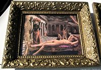 Close-up photo of gilt carved wood frame with surreal art print showing reclining nude woman and skeleton figure in classical setting